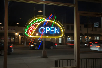Neon sign shaped like a taco with 'OPEN' text on a brick wall.